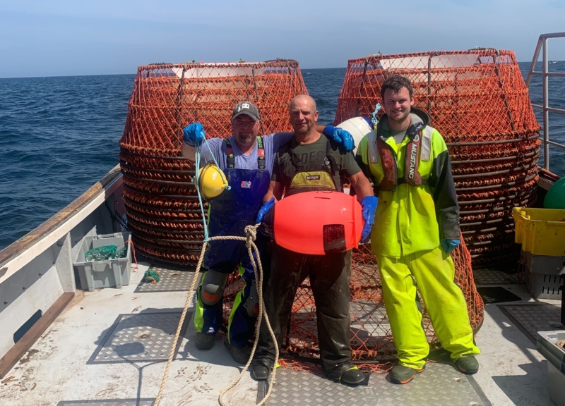 Three fishermen standing on a boat in front of crab traps